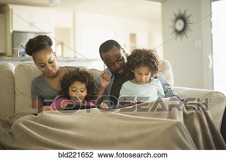 Stock Image - Family using digital tablets on sofa. Fotosearch
