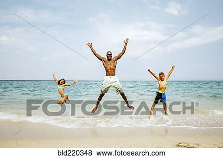 Stock Photo - Father and children jumping for joy on beach. Fotosearch