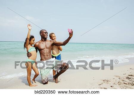 Stock Image - Father and children taking selfie on beach. Fotosearch