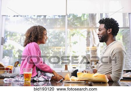 Stock Image - Father and daughter eating in kitchen. Fotosearch