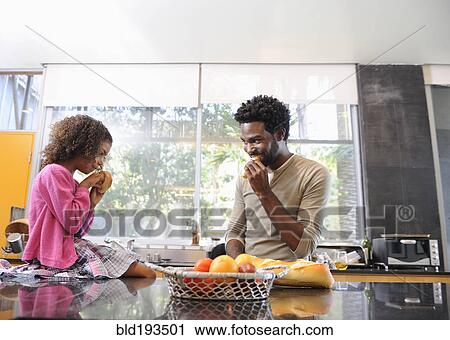 Stock Image - Father and daughter eating in kitchen. Fotosearch