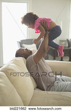 Stock Image - Father and daughter playing on sofa. Fotosearch
