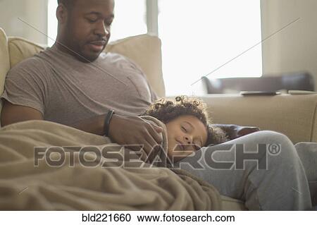 Stock Image - Father and daughter snuggling on sofa. Fotosearch