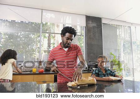 Stock Image - Father and daughters preparing food in kitchen. Fotosearch