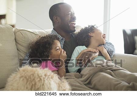 Stock Photography - Father and daughters watching television on sofa. Fotosearch