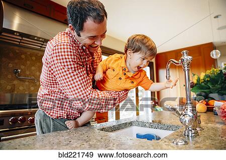 Stock Photo - Father and son playing with faucet in kitchen. Fotosearch