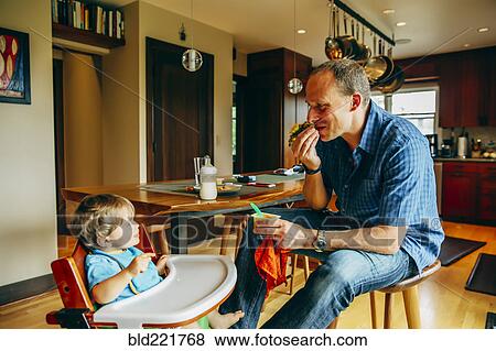 Stock Photo - Father feeding baby son in high chair. Fotosearch
