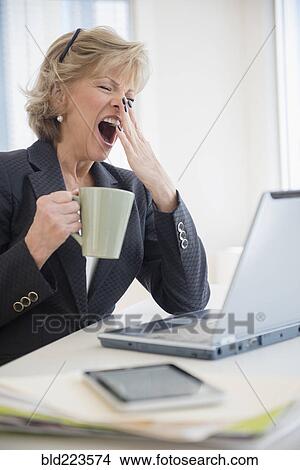 Fatigued Caucasian businesswoman drinking coffee and yawning View Large Photo Image Picture - Fatigued Caucasian businesswoman drinking coffee and yawning. Fotosearch