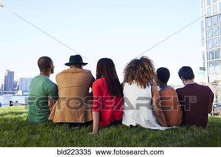 Stock Photography - Friends sitting in grass at waterfront. Fotosearch