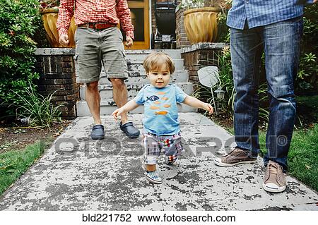 Stock Image - Gay fathers and baby son standing outdoors. Fotosearch
