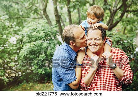 Stock Photography - Gay fathers holding baby son outdoors. Fotosearch
