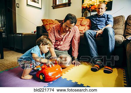 Gay fathers playing with baby son in living room View Large Photo Image Picture - Gay fathers playing with baby son in living room. Fotosearch