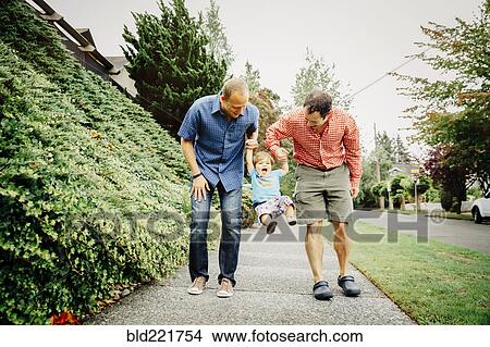 Picture - Gay fathers playing with baby son on sidewalk. Fotosearch