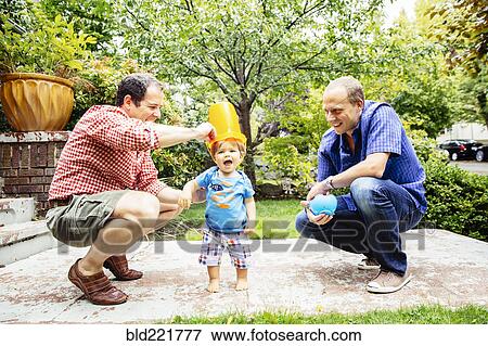 Stock Photo - Gay fathers playing with baby son outdoors. Fotosearch
