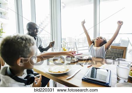 Stock Image - Girl cheering at table in restaurant. Fotosearch