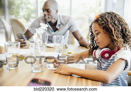 Stock Image - Girl coloring at restaurant table. Fotosearch