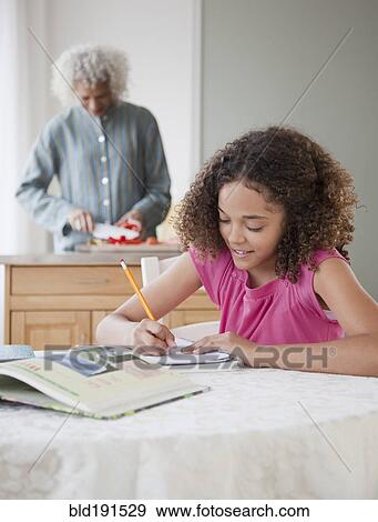 Girl doing homework with grandmother in background View Large Photo Image Stock Photo - Girl doing homework with grandmother in background. Fotosearch
