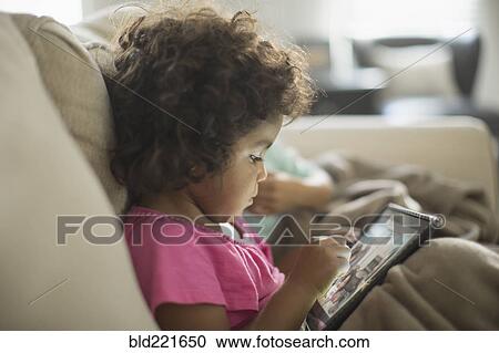 Stock Image - Girl using digital tablet on sofa. Fotosearch