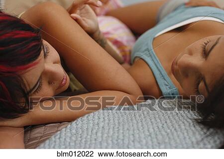 Stock Image - Girlfriends laying on bed together. Fotosearch