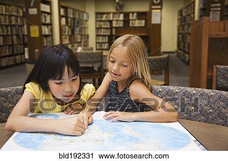 Stock Image - Girls looking at atlas in library. Fotosearch