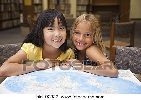 Stock Image - Girls looking at atlas in library. Fotosearch