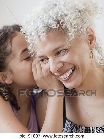 Stock Photo - Granddaughter whispering into grandmother's ear. Fotosearch