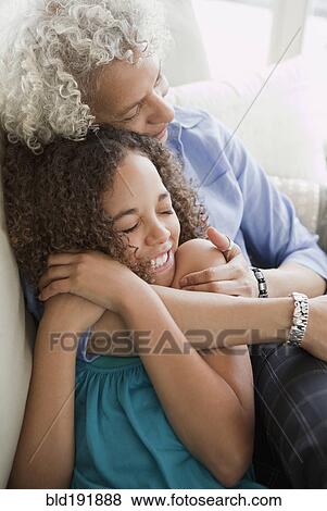 Stock Photo - Grandmother and granddaughter hugging on sofa. Fotosearch