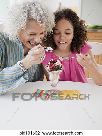 Stock Image - Grandmother and granddaughter sharing ice cream sundae. Fotosearch