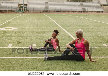 Stock Image - Grandmother and granddaughter stretching on football field. Fotosearch
