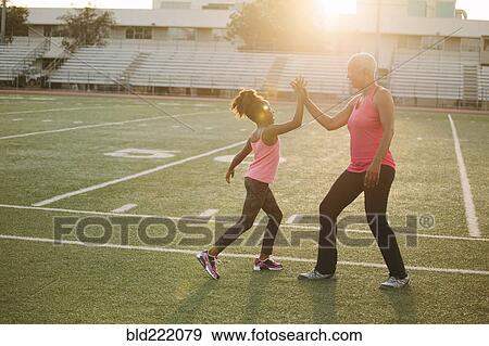 Stock Photo - Grandmother and granddaughter high-fiving on football field. Fotosearch
