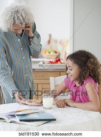 Stock Image - Grandmother serving granddaughter cookies. Fotosearch