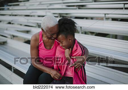 Picture - Grandmother wrapping sweater around granddaughter on bleachers. Fotosearch