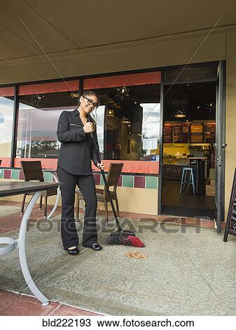 Stock Image - Hispanic business owner sweeping sidewalk. Fotosearch