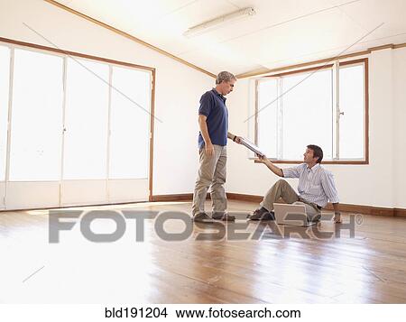 Picture - Hispanic businessman handing paperwork to co-worker in empty office. Fotosearch