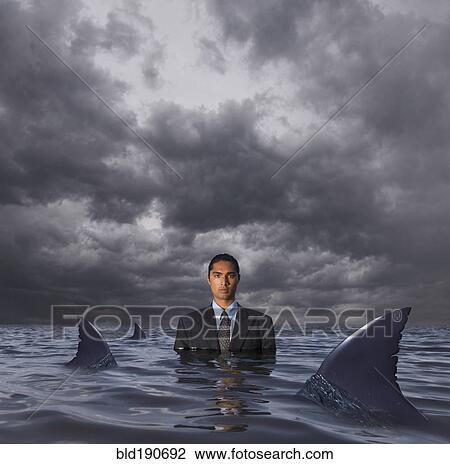 Stock Image - Hispanic businessman standing in water with sharks. Fotosearch