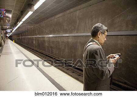 Stock Photograph - Hispanic businessman waiting in subway using cell phone. Fotosearch