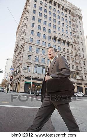 Stock Image - Hispanic businessman walking on urban street. Fotosearch