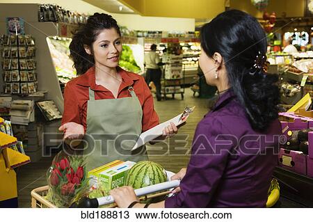 Stock Image - Hispanic clerk helping shopper in grocery store. Fotosearch