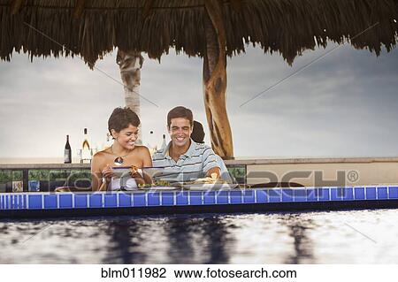 Stock Image - Hispanic couple having dinner at poolside. Fotosearch