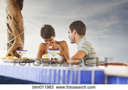 Stock Image - Hispanic couple having dinner at poolside. Fotosearch
