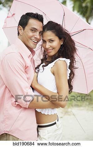 Picture - Hispanic couple hugging under umbrella. Fotosearch