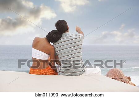 Stock Image - Hispanic couple sitting and looking at ocean. Fotosearch