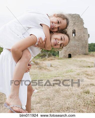 Hispanic girl giving sister piggyback ride near castle ruins View Large Photo Image Picture - Hispanic girl giving sister piggyback ride near castle ruins. Fotosearch