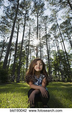 Stock Image - Hispanic girl squatting outdoors. Fotosearch
