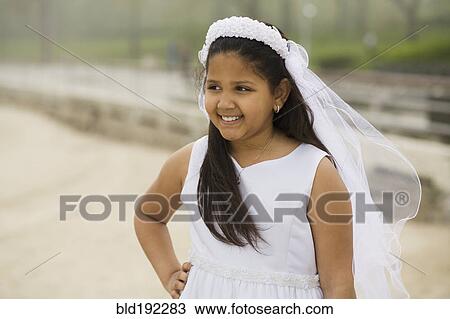 Stock Image - Hispanic girl wearing first communion gown and veil. Fotosearch