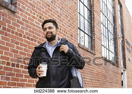 Stock Photo - Hispanic man carrying bag and coffee cup in city. Fotosearch
