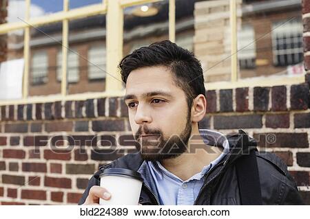 Stock Photo - Hispanic man carrying bag drinking coffee in city. Fotosearch