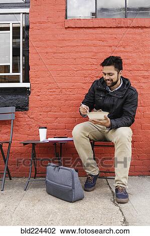 Stock Image - Hispanic man eating bowl of food on sidewalk. Fotosearch