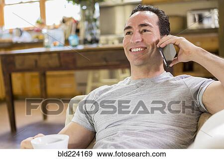 Stock Photo - Hispanic man laying on sofa using cell phone. Fotosearch