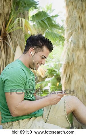 Stock Image - Hispanic man listening to mp3 player in tropical area. Fotosearch